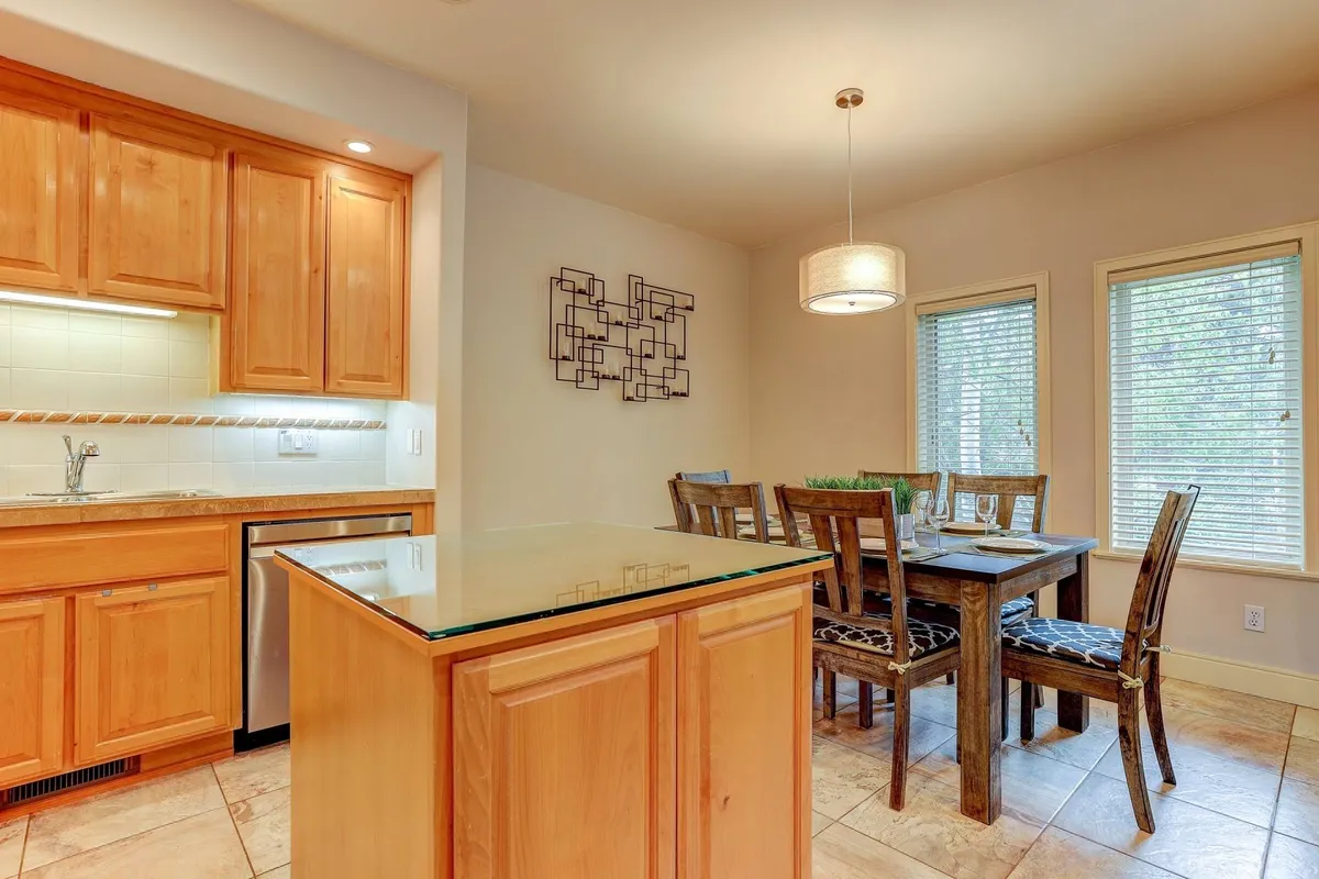A bright, open-concept kitchen and dining area, featuring a central kitchen island and a dining table set beside wide windows. The space flows seamlessly, inviting casual breakfasts, festive dinners, or simply gathering together.