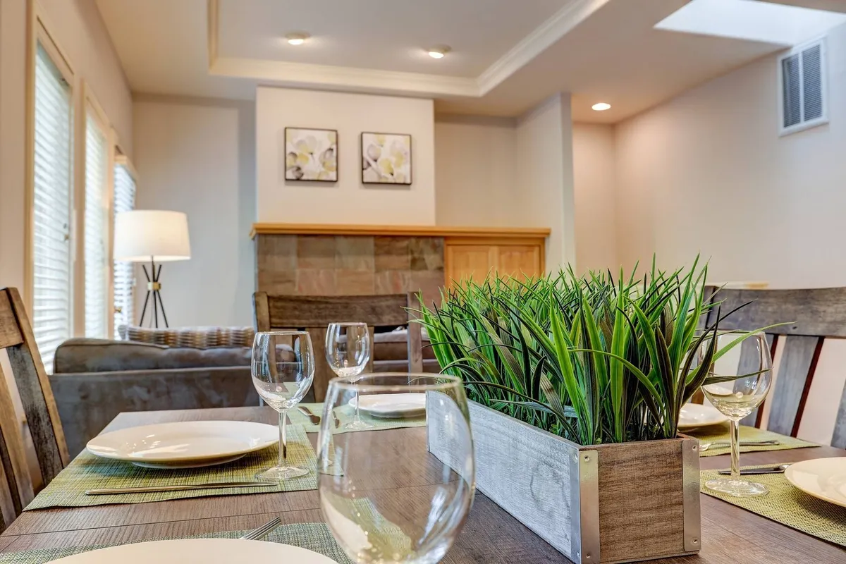 A stylish dining table set with plates and glasses, a lush greenery centerpiece, and tasteful wall art provide a welcoming backdrop for shared meals and laughter. The space exudes warmth and connection.