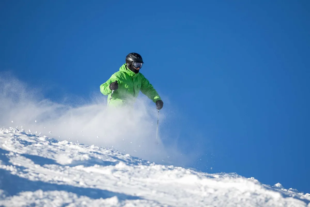 An exterior winter scene featuring a skier gliding down snowy slopes against a dramatic mountain backdrop. The environment is filled with energy and excitement, capturing the adventure and outdoor recreation for which Bend is known.