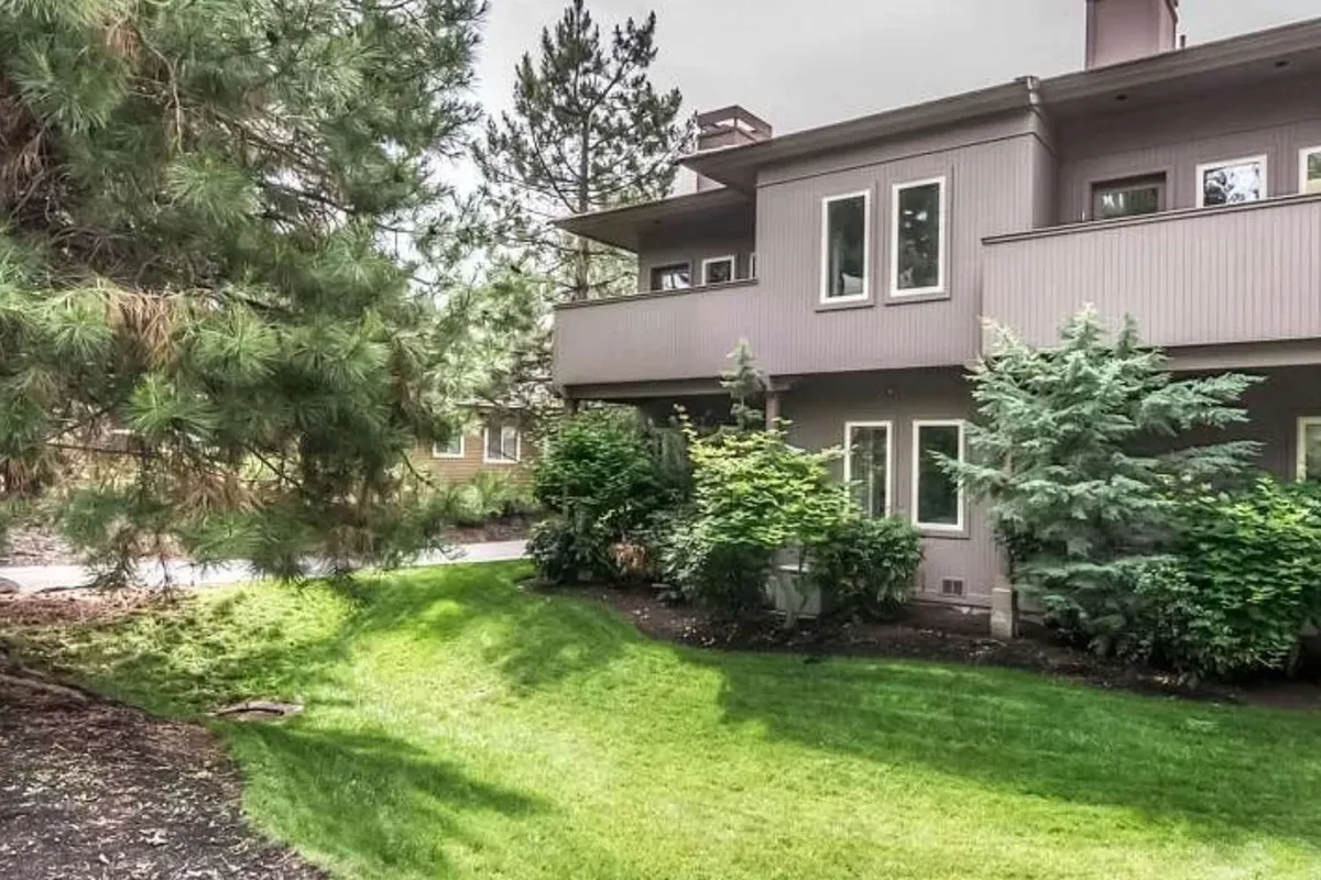 Here, the exterior of the townhome is shown amidst lush greenery and a well-maintained lawn, highlighting the modern architecture and resort-style landscaping. The scene exudes a sense of tranquility and connection to nature, echoing the proximity to Broken Top Golf Club and the inviting outdoor lifestyle referenced in the section.