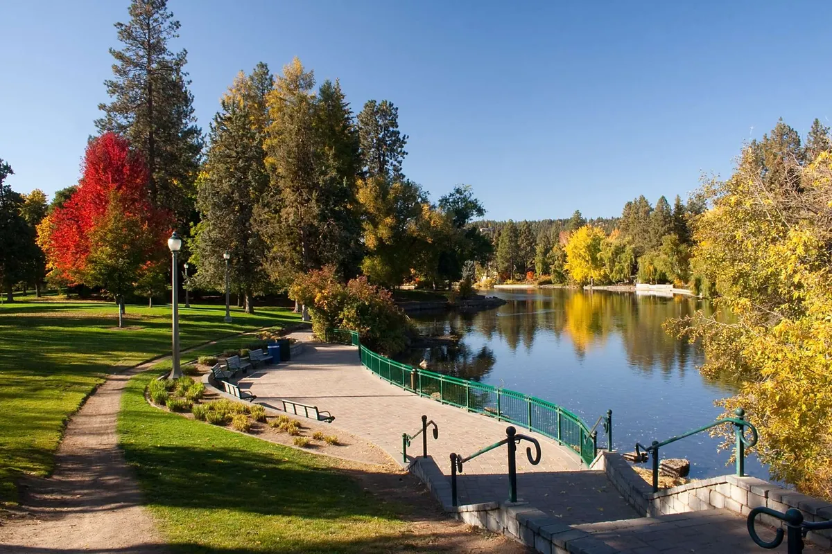 A peaceful riverside scene with a calm river bordered by colorful trees and a scenic pathway, inviting visitors to relax or explore the outdoors.