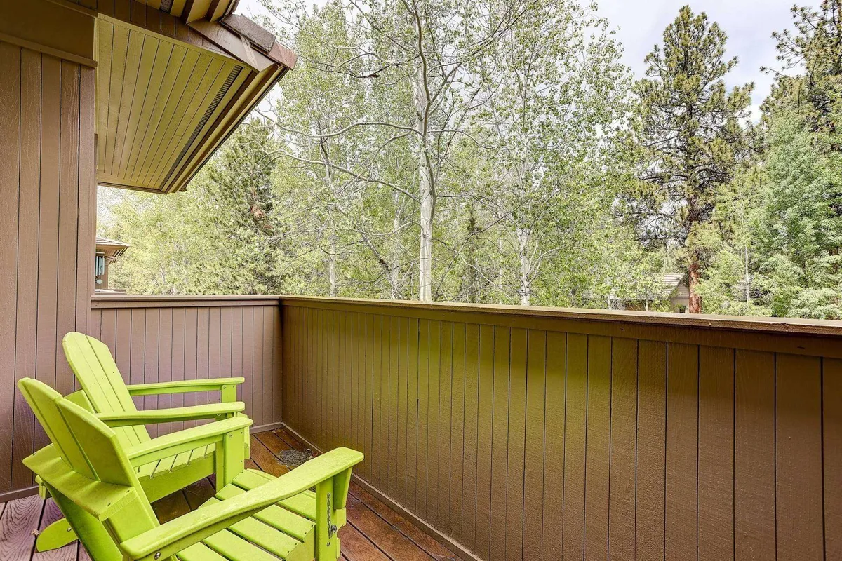 This image depicts a serene private balcony featuring green Adirondack chairs positioned to overlook lush natural greenery and framed by a wooden railing. The space exudes tranquility, with the chairs inviting residents or guests to relax, read, or simply enjoy the peaceful ambiance. The setting is perfect for stargazing, morning coffee, or quiet contemplation, directly connecting the interior space to the outdoors.