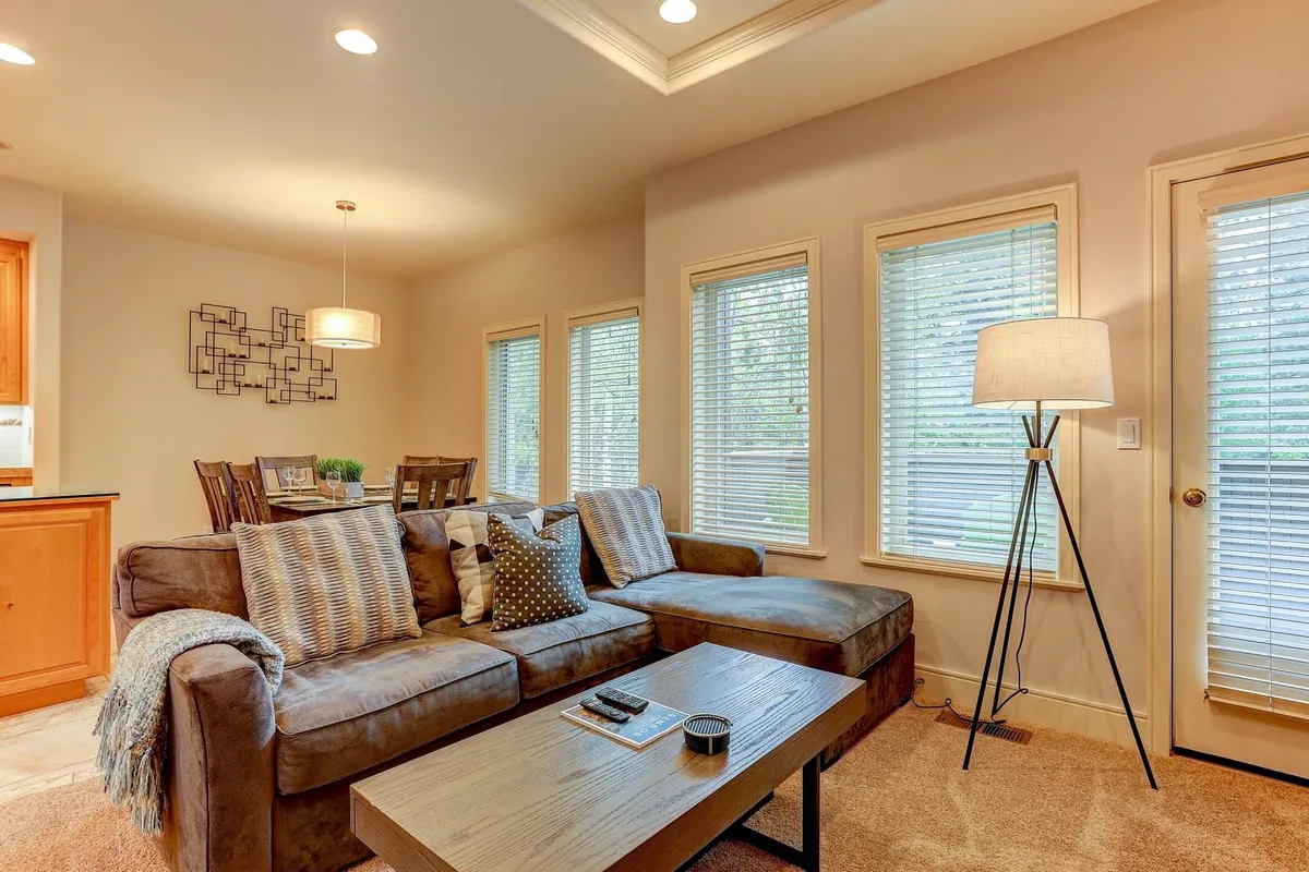 A cozy living room featuring a plush sofa, a coffee table, a floor lamp, and large windows that invite in natural light. The seating is arranged to encourage conversation and relaxation, with gentle sunlight creating a warm, inviting atmosphere.