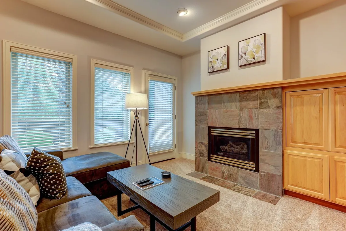 The image showcases a cozy living room featuring a comfortable sofa, a warm stone fireplace, a sturdy wooden coffee table, and decorative art on the wall. The ambiance is inviting and perfect for relaxation or socializing with loved ones.