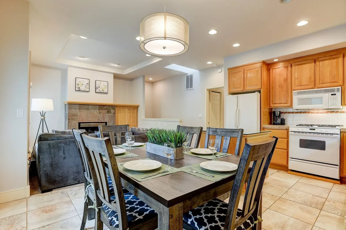 An open-plan dining area with a table set for a meal, surrounded by kitchen cabinets and a cozy seating area. Soft lighting and thoughtful decor create a warm, inviting space ideal for shared meals and celebrations.