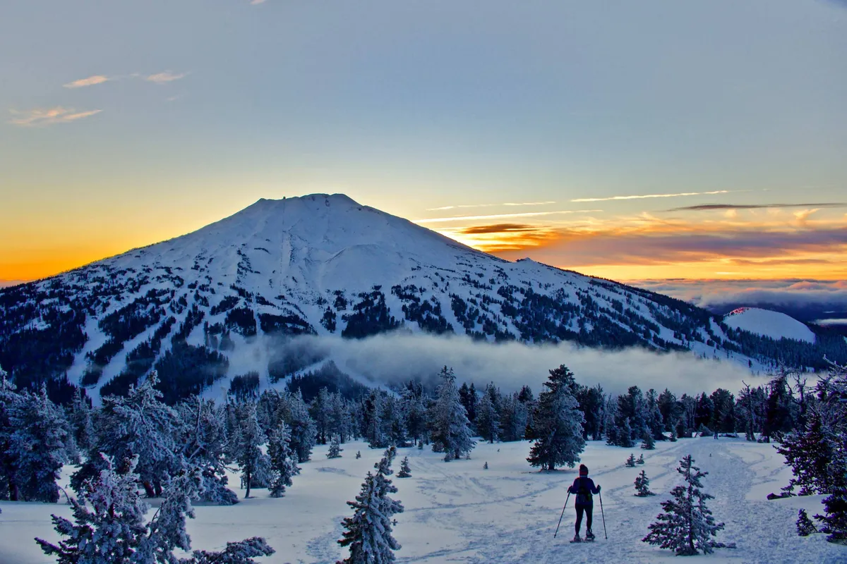 This scenic view captures a snow-covered mountain at sunset, with ski tracks winding through the untouched snow. The composition highlights Central Oregon's natural beauty and outdoor allure, pairing the tranquility of the balcony with the grandeur of the surrounding landscape.